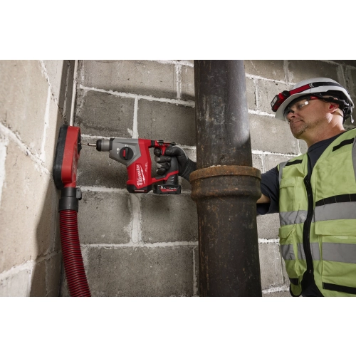 Milwaukee M12 FHAC16 z nasadką odsysającą i wężem wierci w ścianie z bloczków obok rury (ujęcie 2)