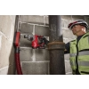 Milwaukee M12 FHAC16 z nasadką odsysającą i wężem wierci w ścianie z bloczków obok rury