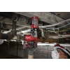 Milwaukee M12 FHAC16 z przystawką odsysającą wierci nad głową w stropie między rurami instalacji