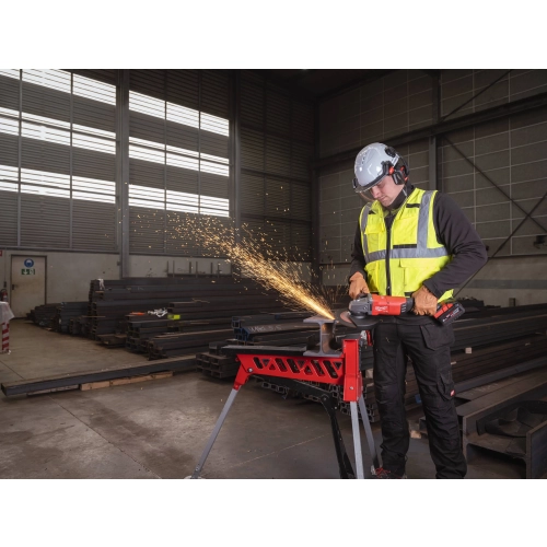 Pracownik w kasku z Milwaukee M18 ONEFLAG230XPDB w hali konstrukcji stalowych