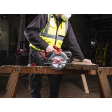 Pracownik tnie Milwaukee M18 FCS66GR3 kantówkę na kozłach, w tle maszyny stolarskie