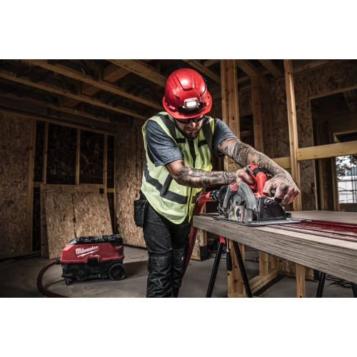 Pracownik w kasku tnie Milwaukee M18 FCS66GR3 długą płytę na szynie z odkurzaczem w tle