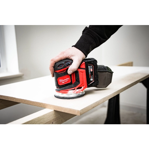 Milwaukee M18 BOS125 szlifuje drewniany blat przy krawędzi