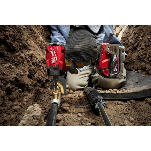 Pracownik w wykopie dokręca Milwaukee M18 FIW2F12 śrubę przy rurze