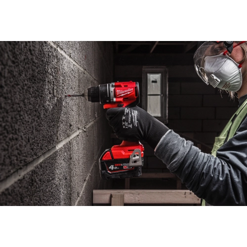 Pracownik w masce wierci Milwaukee M18 BLPDRC w ścianie z bloczków
