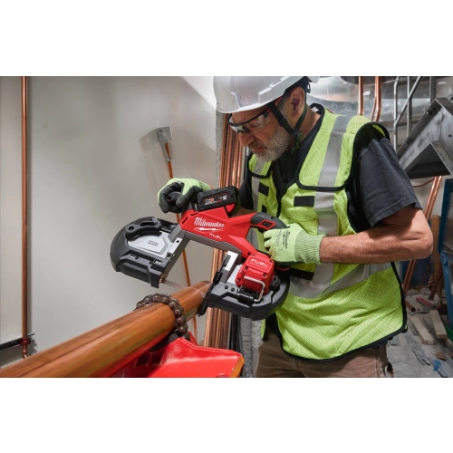 Instalator w kasku tnie Milwaukee M18 FBS127 grubą rurę miedzianą trzymaną ręką