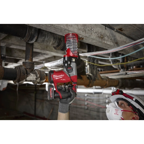 Milwaukee M12 FHAC16 z przystawką odsysającą wierci nad głową w stropie między rurami instalacji
