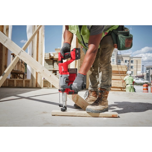 Pracownik wierci Milwaukee M18 BLHACD26 przez drewnianą podwalinę w betonową płytę