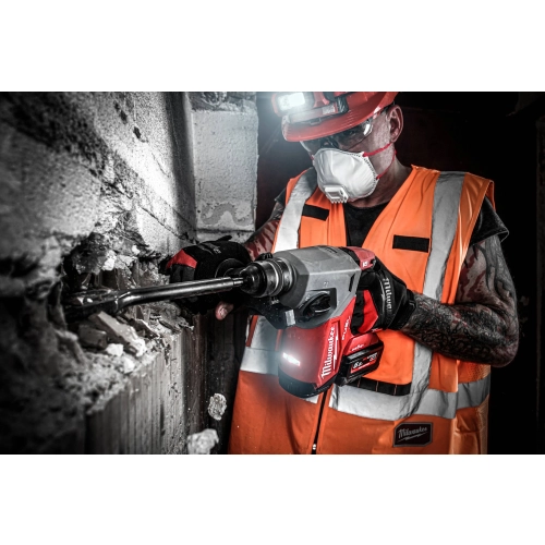 Pracownik z latarką czołową kuje Milwaukee M18 ONEFH dłutem płaskim SDS-Plus w betonowym słupie