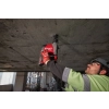Pracownik wierci Milwaukee M18 FHAFOH16 pionowo w górę w surowym betonowym stropie