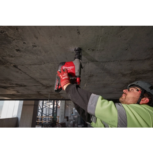 Pracownik wierci Milwaukee M18 FHAFOH16 pionowo w górę w surowym betonowym stropie