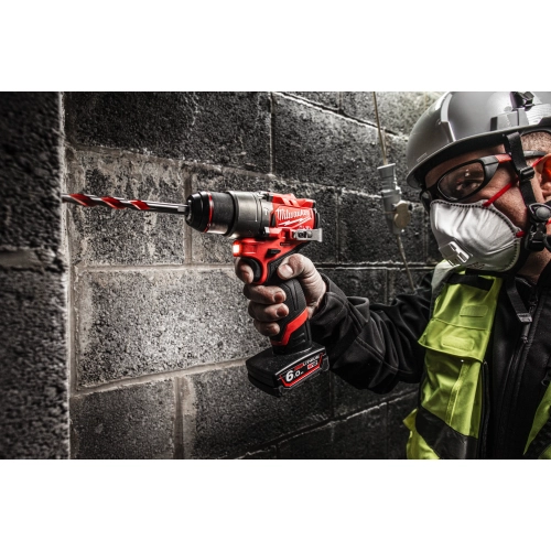 Pracownik w masce wierci Milwaukee M12 FPD2 wiertłem do betonu w ścianie z bloczków