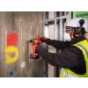 Pracownik w kasku wierci Milwaukee M18 ONEPD3 w betonowej ścianie obok profili