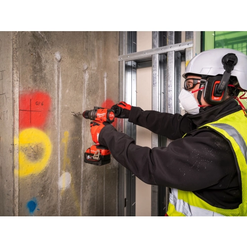 Pracownik w kasku wierci Milwaukee M18 ONEPD3 w betonowej ścianie obok profili