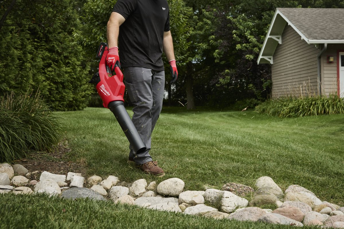 Mężczyzna zdmuchuje ścinki trawy z obrzeża trawnika przy kamieniach dmuchawą Milwaukee M18 BLBLO