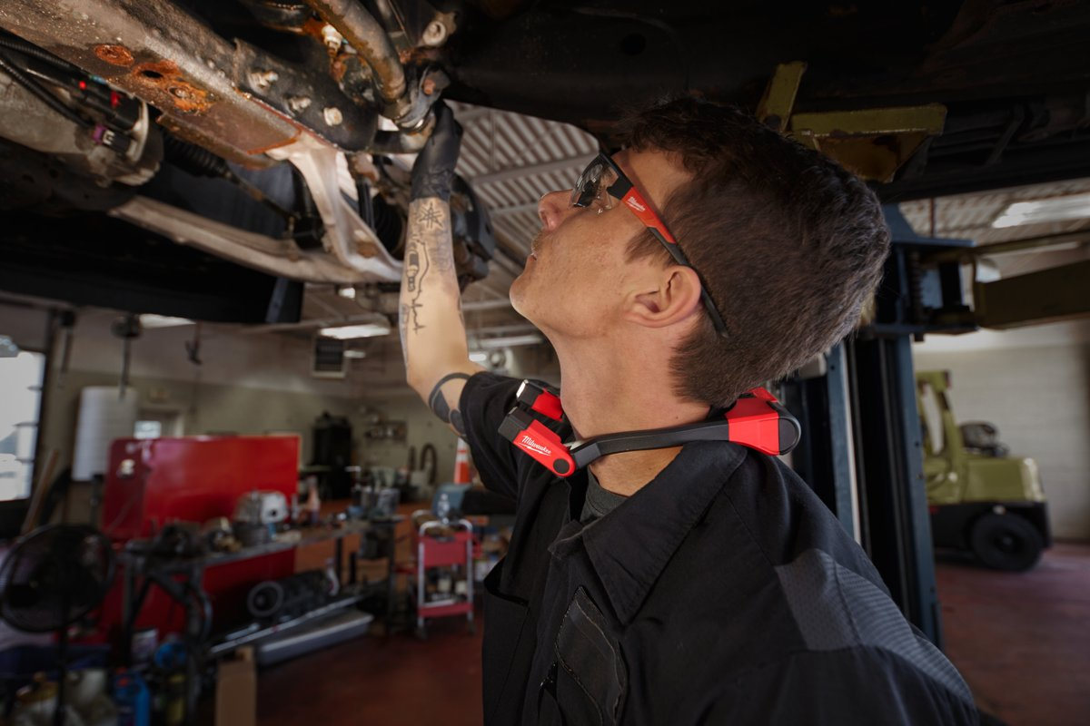 Mechanik pod samochodem na podnośniku z latarką Milwaukee L4 NL400 skierowaną w górę