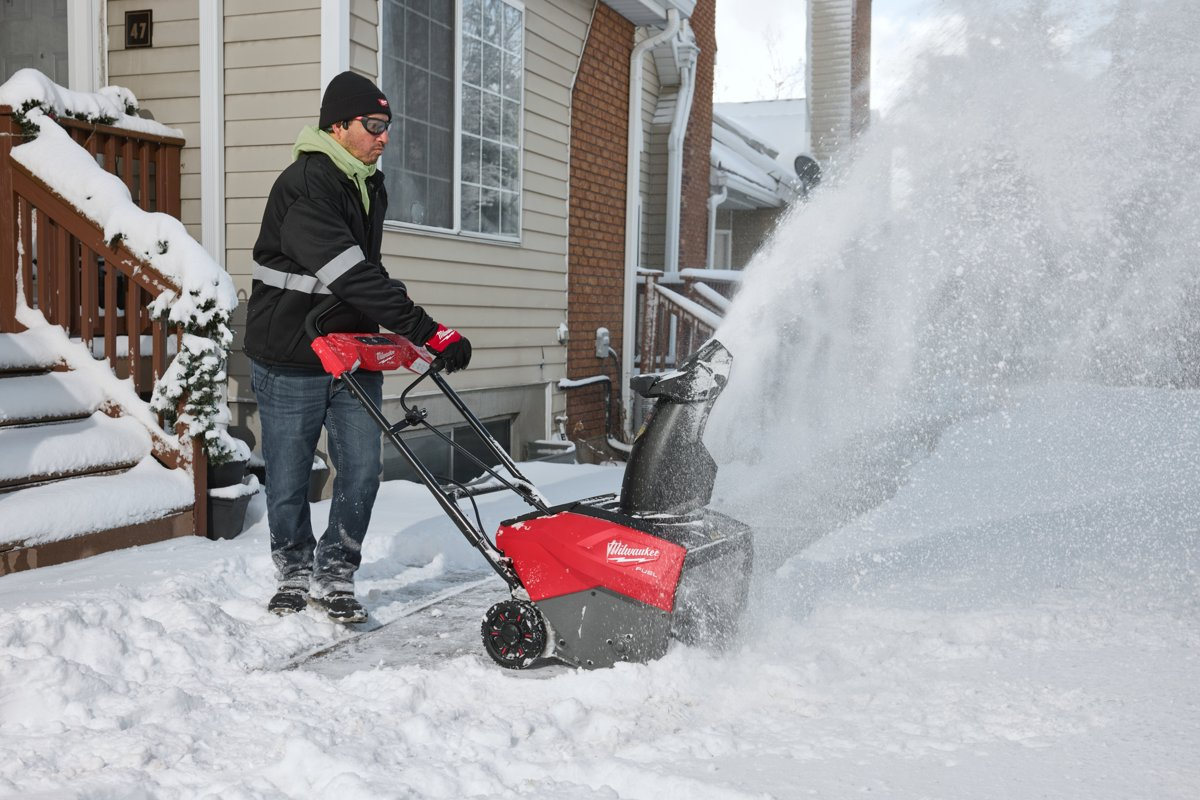 Mężczyzna odśnieża wejście przy schodach domu odśnieżarką Milwaukee M18 FUEL F2SSBL