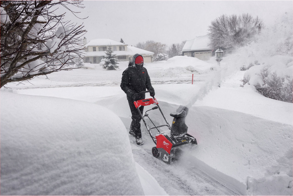 Mężczyzna przebija się odśnieżarką Milwaukee M18 FUEL przez głęboki śnieg przy zaspie