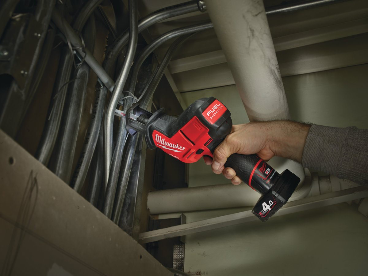 Elektryk tnie rurę osłonową przy suficie piłą szablastą Milwaukee M12 FUEL HACKZALL