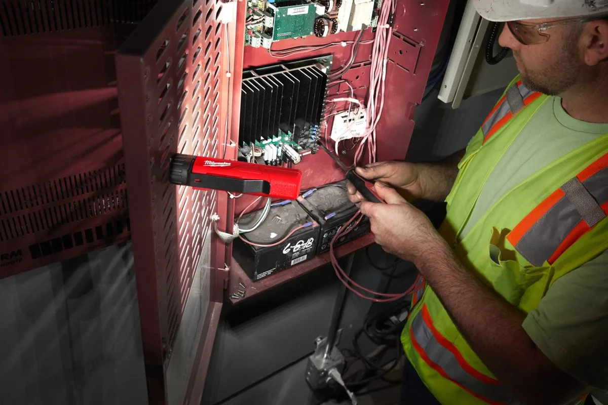 Elektryk podłącza przewody w szafie sterowniczej przy świetle latarki FL-LED