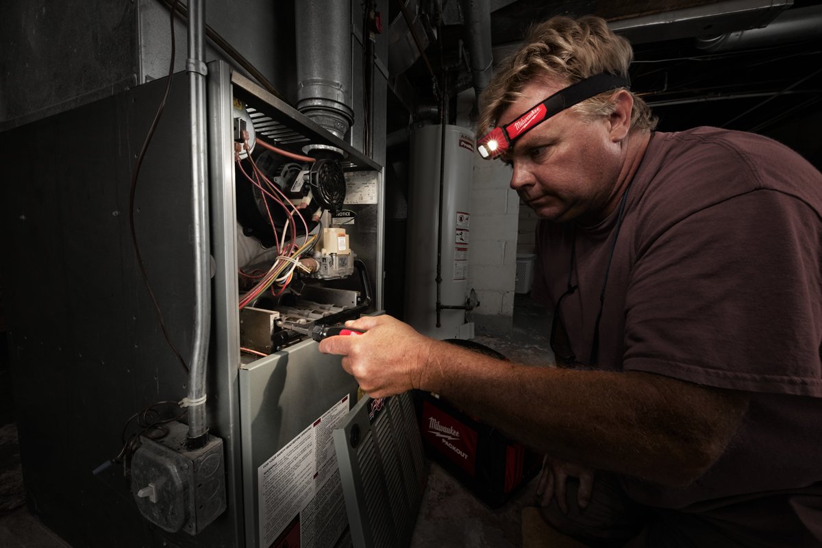 Serwisant z latarką czołową MILWAUKEE na głowie pracuje przy instalacji pieca