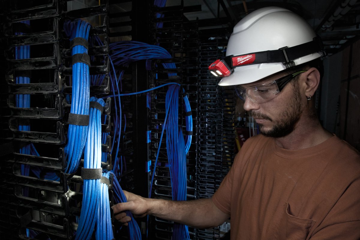 Instalator w kasku z latarką czołową MILWAUKEE porządkuje kable w serwerowni