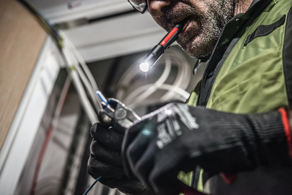 Instalator trzyma latarkę IR PL250 w zębach i pracuje obiema rękami