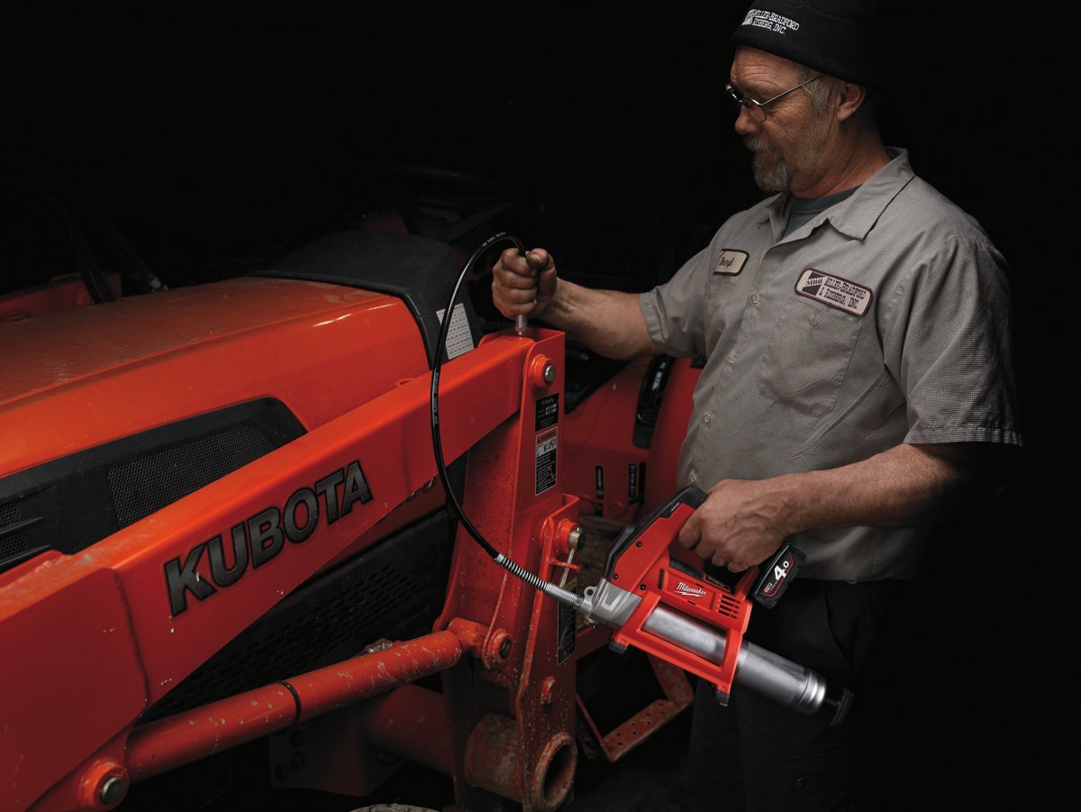 Mechanik smaruje akumulatorową smarownicą MILWAUKEE ramię ładowacza czerwonego ciągnika