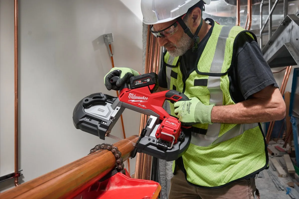 Instalator w kasku tnie M18 FBS127 grubą rurę miedzianą trzymaną ręką