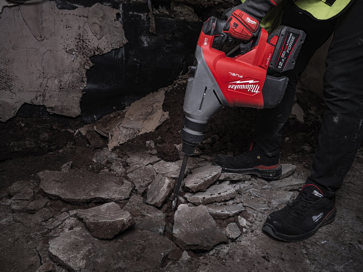 Pracownik kuje M18 FHACO745 dłutem SDS-Max betonową posadzkę, wokół odłamki