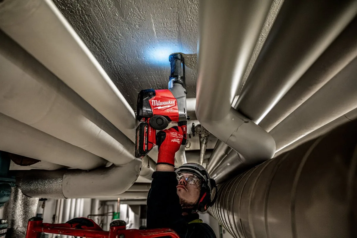 M18 FHAFOH16 z włączoną diodą LED wierci nad głową między rurami instalacji