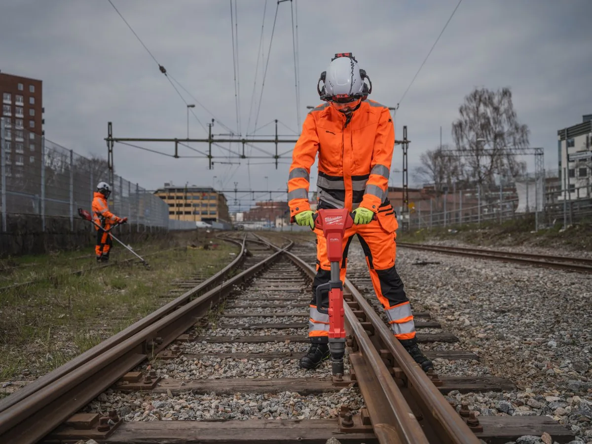 Pracownik kolejowy w pomarańczowym ubraniu dokręca M18 FHIWF1R śrubę w torze na stojąco
