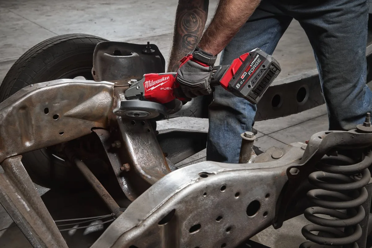 Mechanik szlifuje szlifierką kątową MILWAUKEE element zawieszenia pojazdu