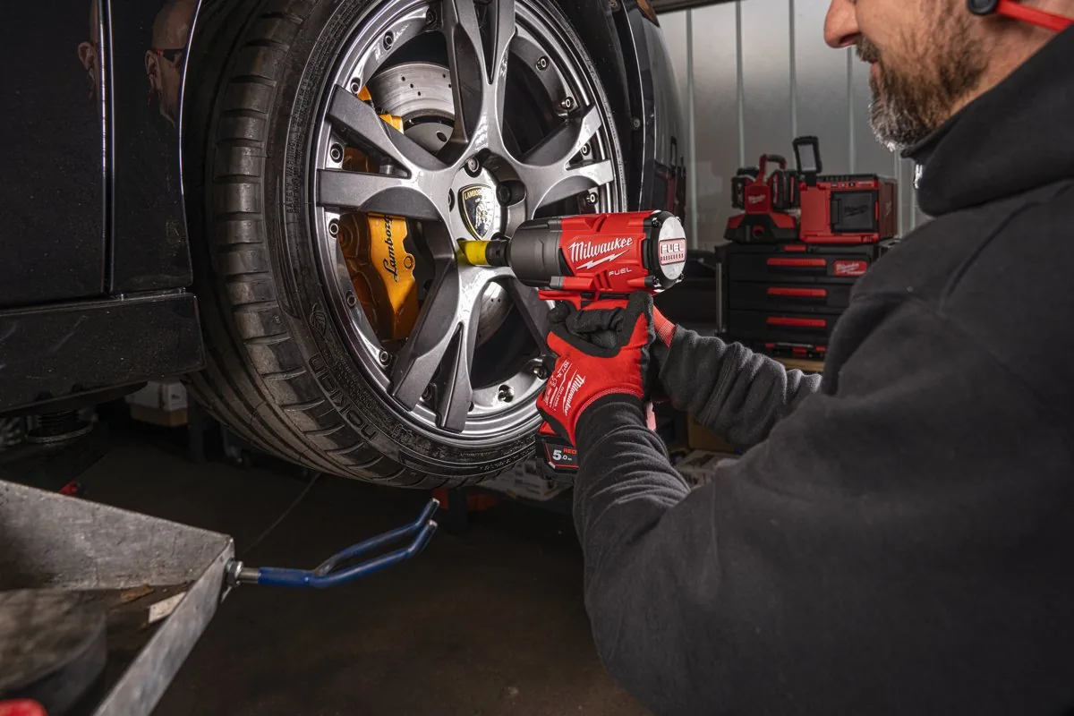 Mechanik odkręca kluczem udarowym MILWAUKEE M18 śruby koła samochodu w warsztacie