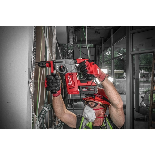 Pracownik w kasku wierci Milwaukee M18 BLHX nad głową przy nadprożu okna