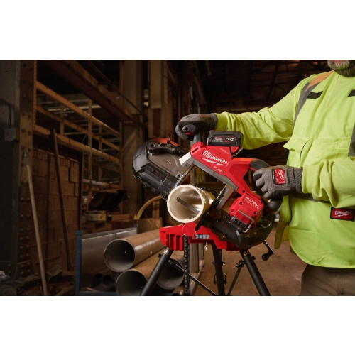 Pracownik tnie Milwaukee M18 FBS127DO rurę na stojaku w hali obok stosu rur