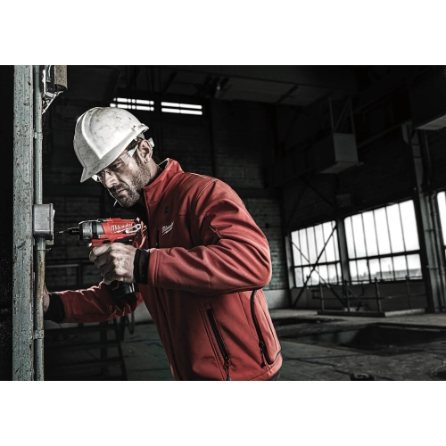 Elektryk w kasku wkręca Milwaukee M12 CD w rozdzielni na ścianie hali